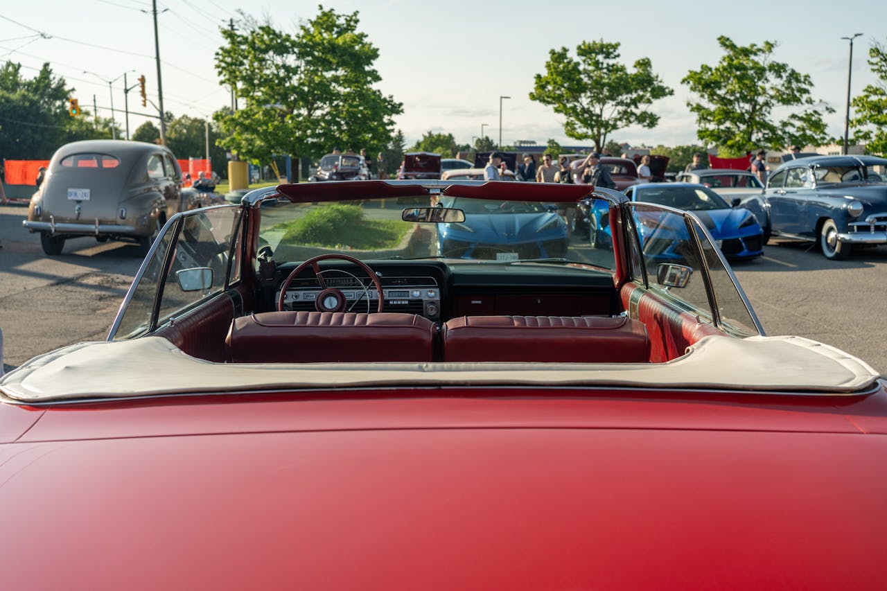 home-hero Rear view of a classic red convertible at a lively outdoor car show.