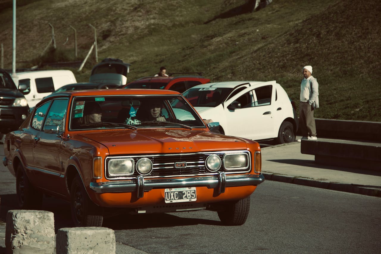 team-05 Classic orange Ford car parked outdoors with visible license plate and surrounding vehicles.